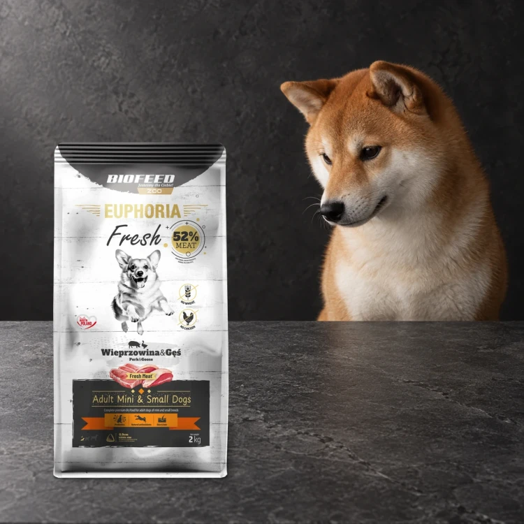 Worek 2 kg karmy Euphoria Fresh z wieprzowiną i gęsią dla dorosłych psów mini i małych ras obok psa na ciemnym tle.