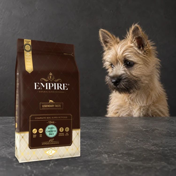 Worek karmy EMPIRE Legendary Taste Puppy Growth Diet dla szczeniąt małych i średnich ras 12 kg obok szczeniaka cairn terriera na ciemnym tle