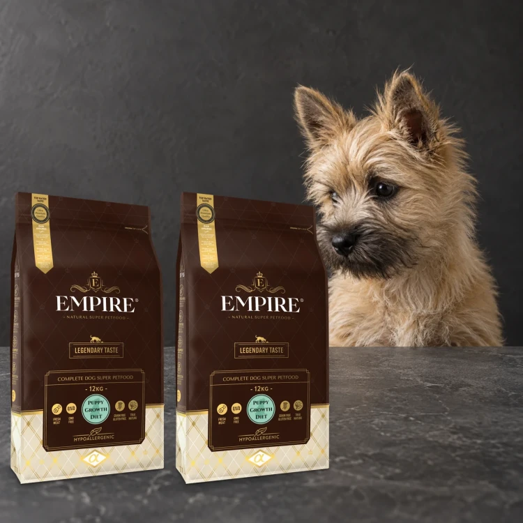 Dwa worki karmy EMPIRE Legendary Taste Puppy Growth Diet dla szczeniąt małych i średnich ras po 12 kg obok szczeniaka cairn terriera na ciemnym tle
