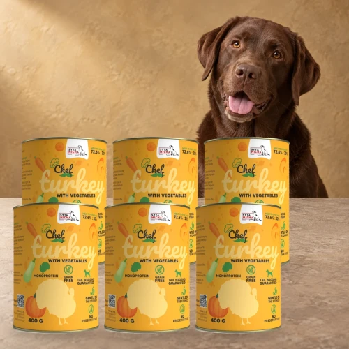 Sześć puszek karmy Syta Micha Indyk z warzywami 6 × 400 g obok psa rasy Labrador retriever na tle w kolorach opakowania
