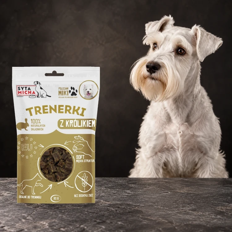 Trenerki Syta Micha z królikiem 80 g obok psa na ciemnym tle.