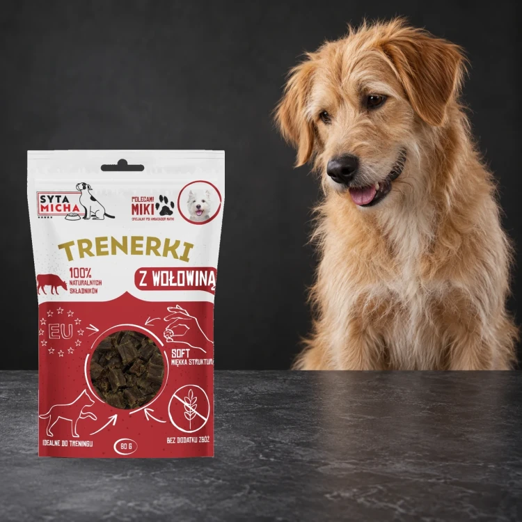 Trenerki Syta Micha z wołowiną 80 g obok psa na ciemnym tle.