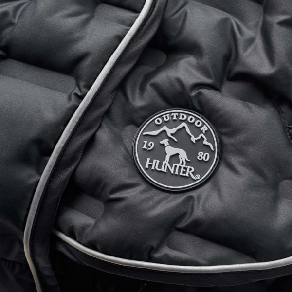 Okrągły emblemat Hunter Outdoor na czarnym pikowanym materiale kurtki Monaco, obok jasna lamówka
